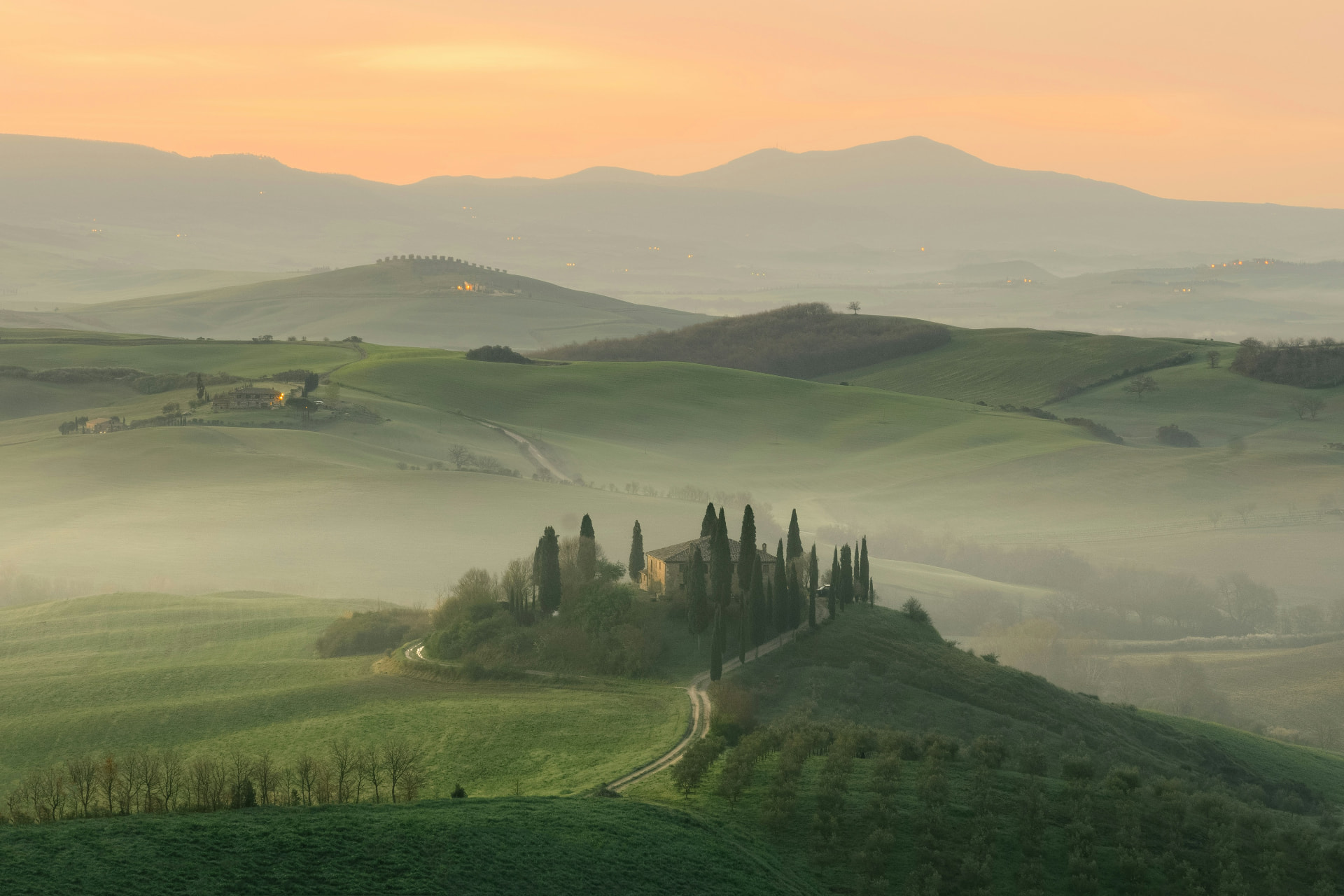 Mist over rolling Tuscan hills at sunrise with a cypress-lined farmhouse.
