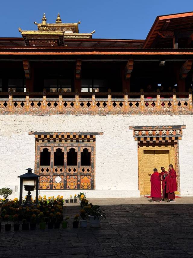 Monks beside the gilded doors of a Bhutanese dzong with whitewashed walls, Punakha, Bhutan.