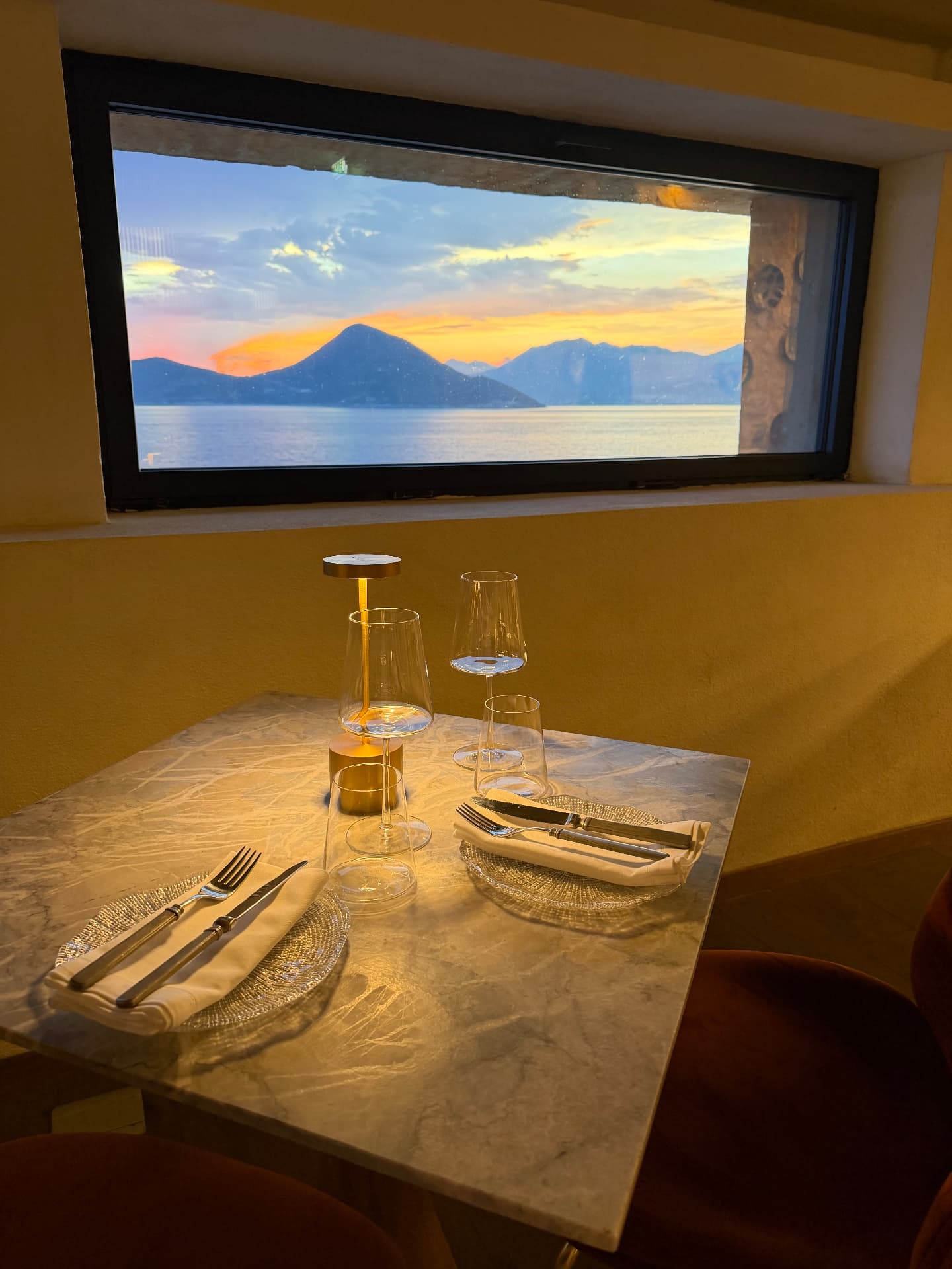 Candlelit dinner table at Mamula Island framing a sunset view over the Bay of Kotor mountains.