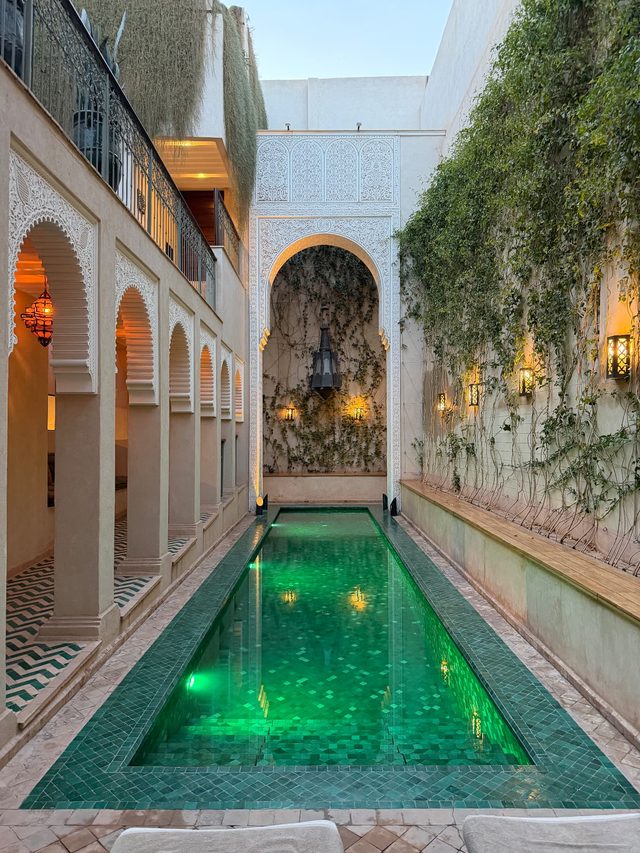 Riad courtyard with a green zellige-tiled pool and lanterns in the Marrakech medina.