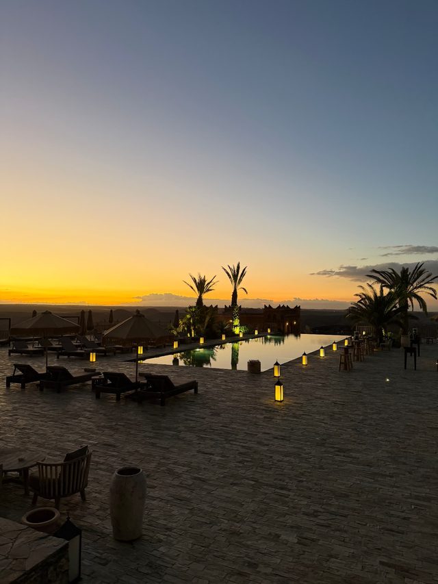 Sunset over a lantern-lined pool terrace at a desert hotel in the Agafay Desert near Marrakech.