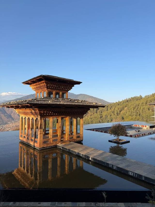 Traditional wooden pavilion in the reflecting pool at Six Senses Thimphu, Bhutan, with forested mountains behind. Traditional wooden pavilion in the reflecting pool at Six Senses Thimphu, Bhutan, with forested mountains behind.