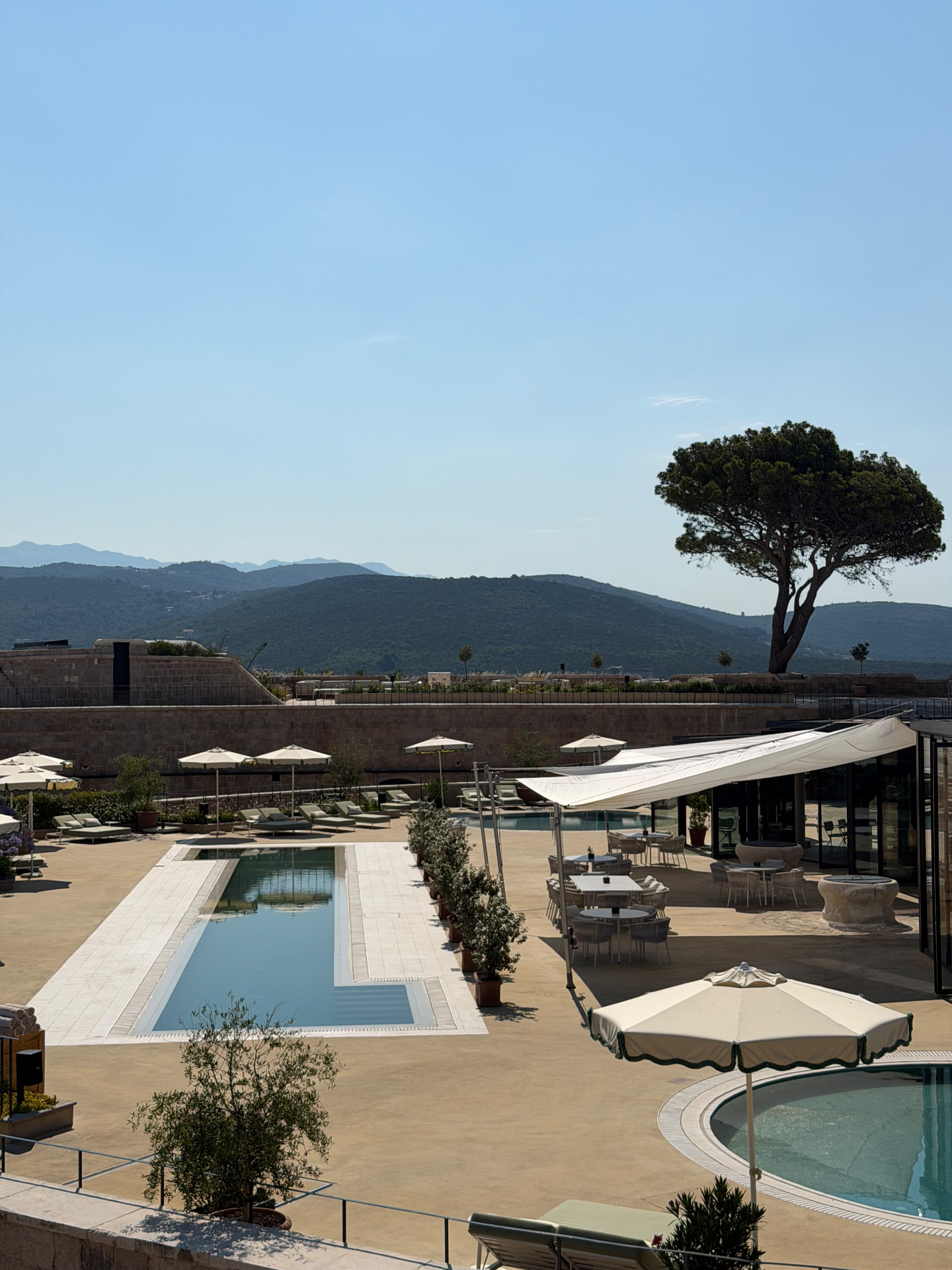 Terrace with three pools and loungers looking towards the mountains above the Bay of Kotor at Mamula Island.